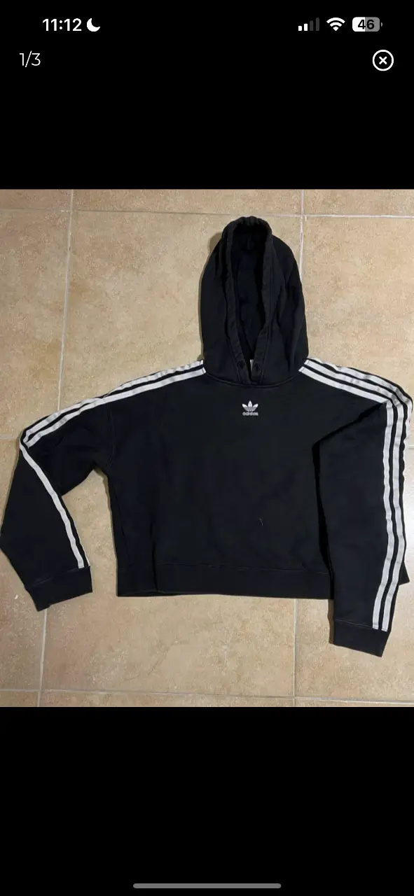Buzo Adidas negro con las clásicas tres tiras blancas en las mangas. Corte crop, ideal para un look deportivo y casual.