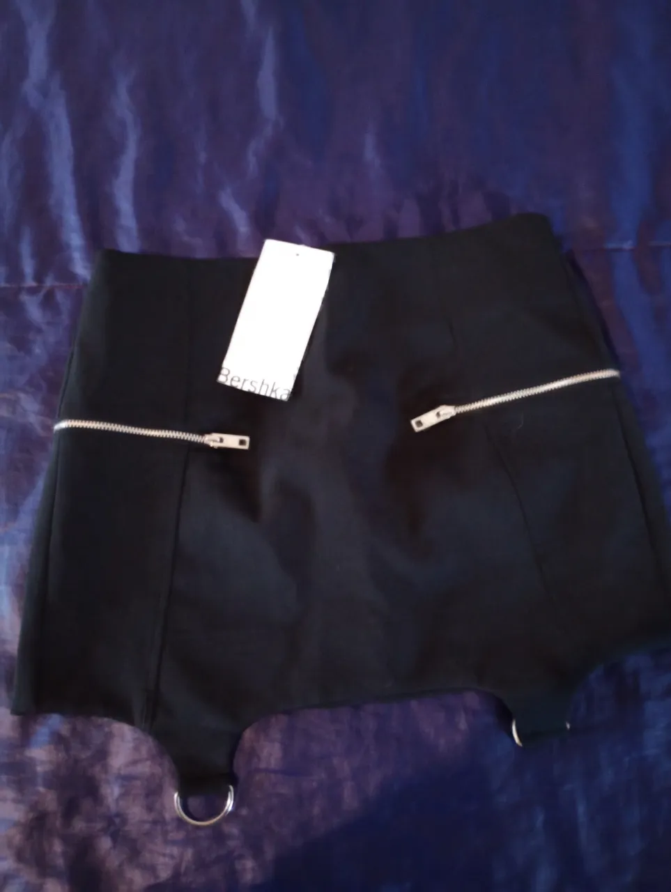 Minifalda negra de Bershka con detalles de cierre y argollas. Ideal para un look moderno y audaz.