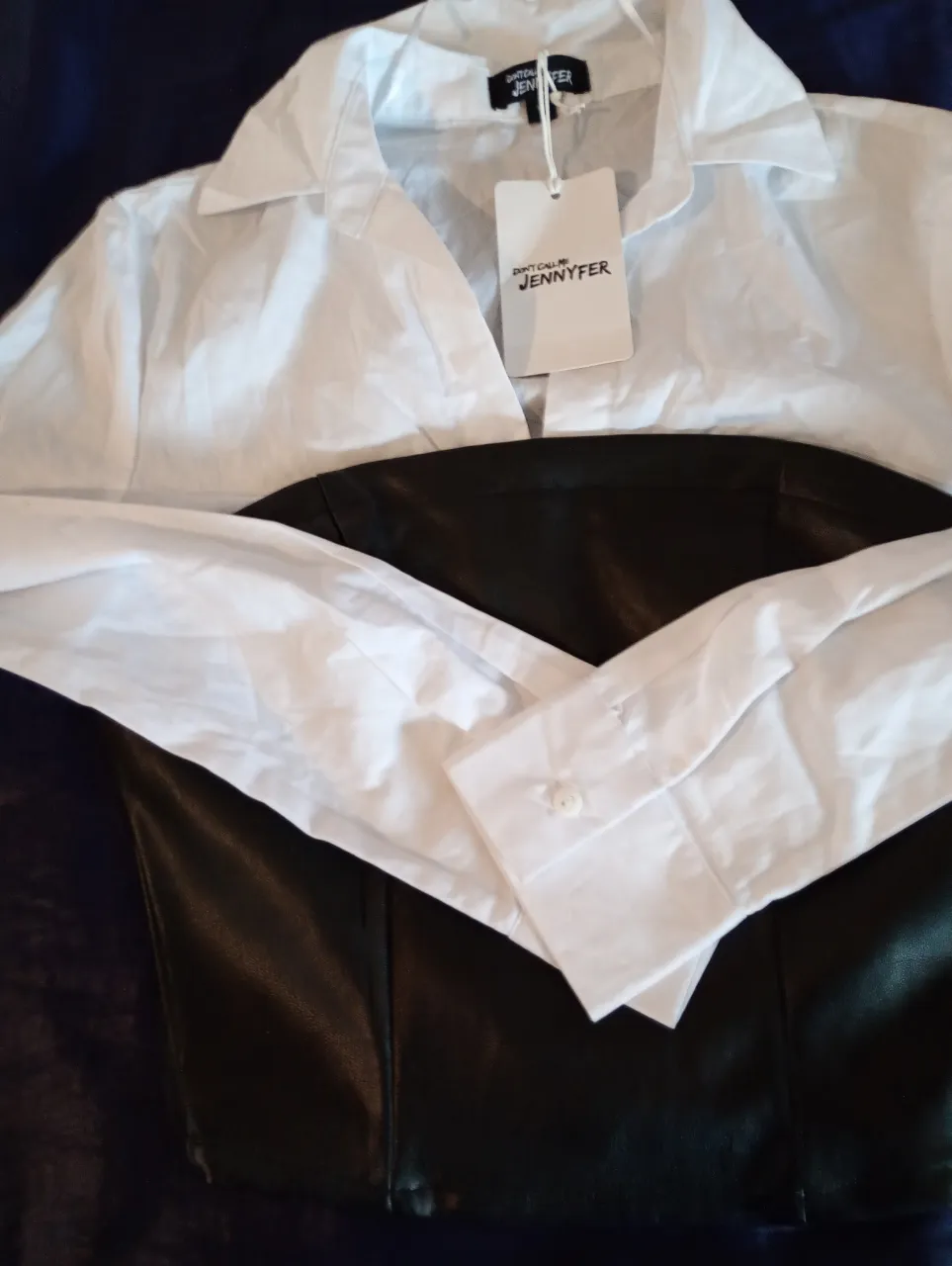 Blusa blanca con cuello y mangas largas, combinada con un top negro de cuero sintético. Ideal para un look elegante y moderno.