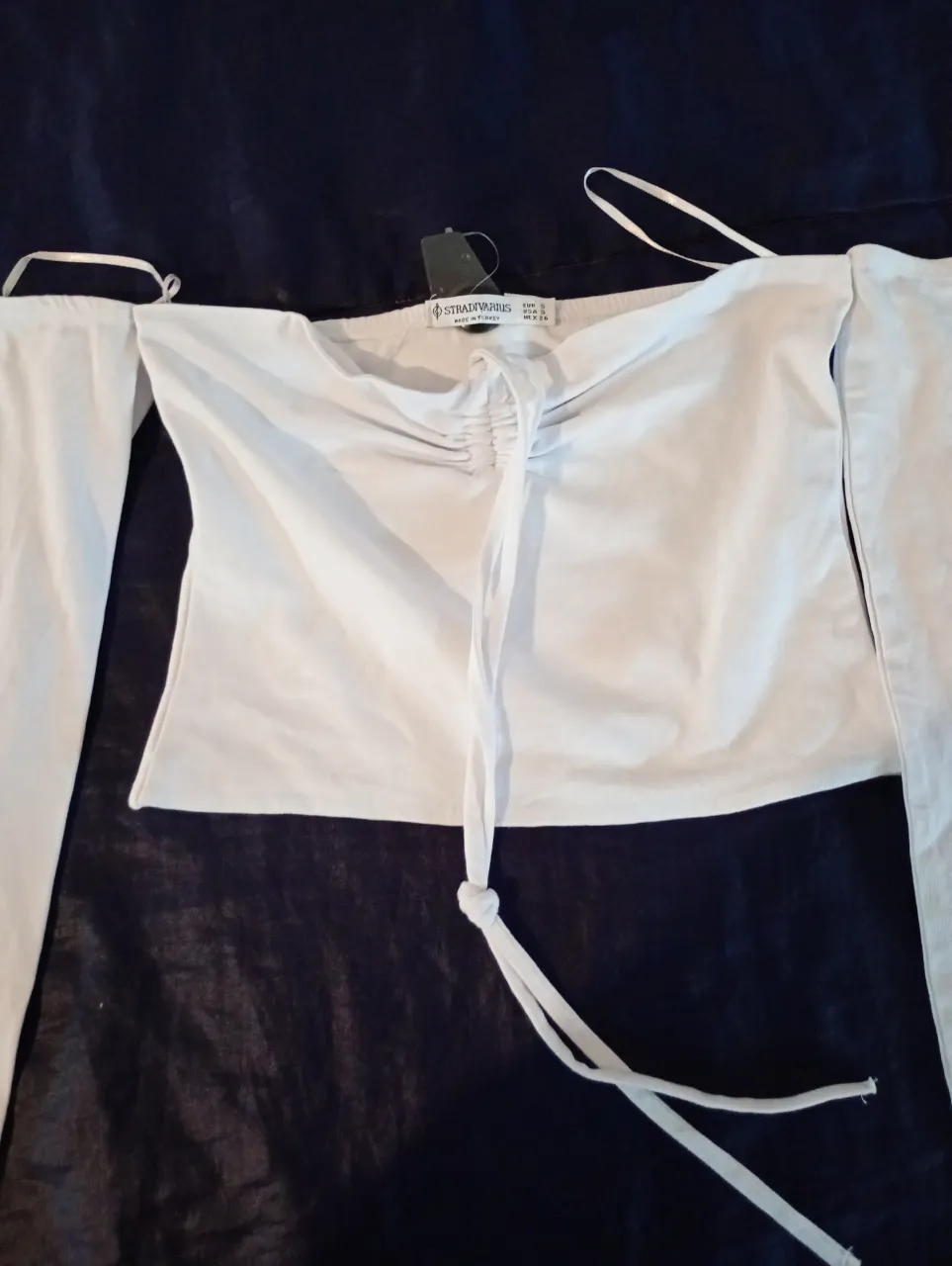 Blusa blanca de mujer, con mangas largas y detalle fruncido en el centro del pecho. Ideal para un look elegante y moderno.