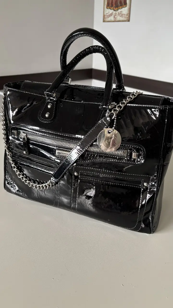 Cartera negra de charol con detalles plateados (niquel) y cadena. Ideal para un look elegante y sofisticado.