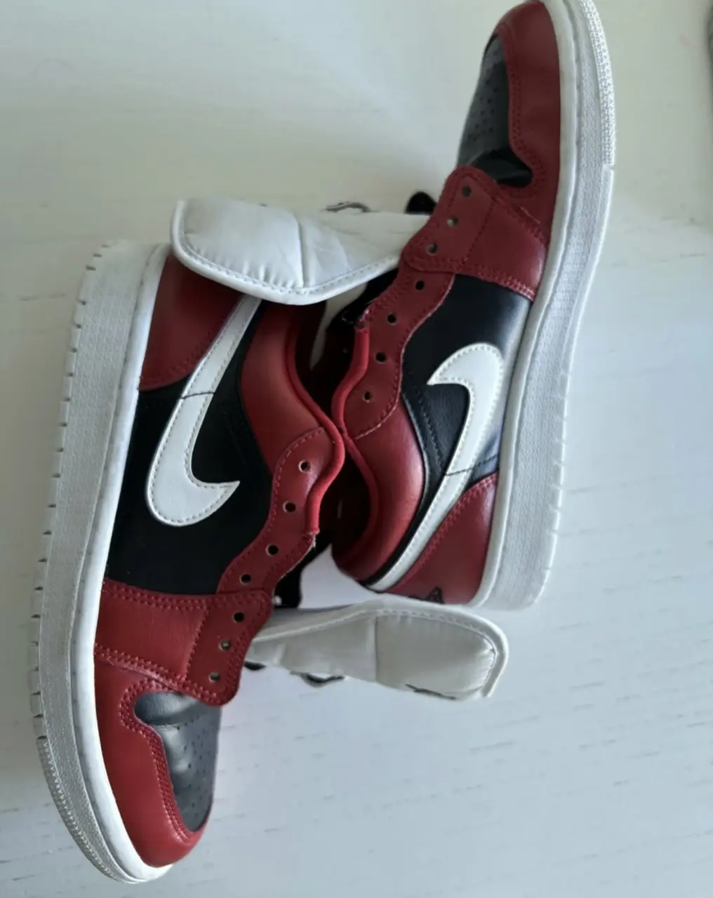 Zapatillas Air Jordan 1 Low, combinan cuero rojo, negro y blanco. Diseño icónico con el logo de Air Jordan en la parte trasera y el logo de Nike en el lateral. Ideales para un look urbano y deportivo.