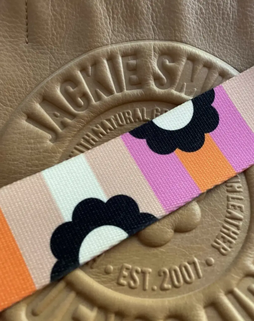 Cartera Jackie Smith de cuero marrón con correa estampada. Diseño con el logo de la marca en relieve y forro interior a rayas. Ideal para un look casual y con estilo.