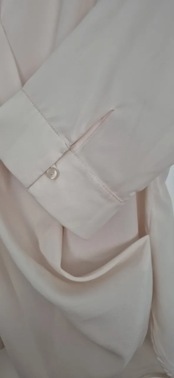 Blusa cruzada color crudo, con mangas 3/4 y detalle de botón en puño. Diseño elegante y moderno, ideal para lucir sofisticada en cualquier ocasión.