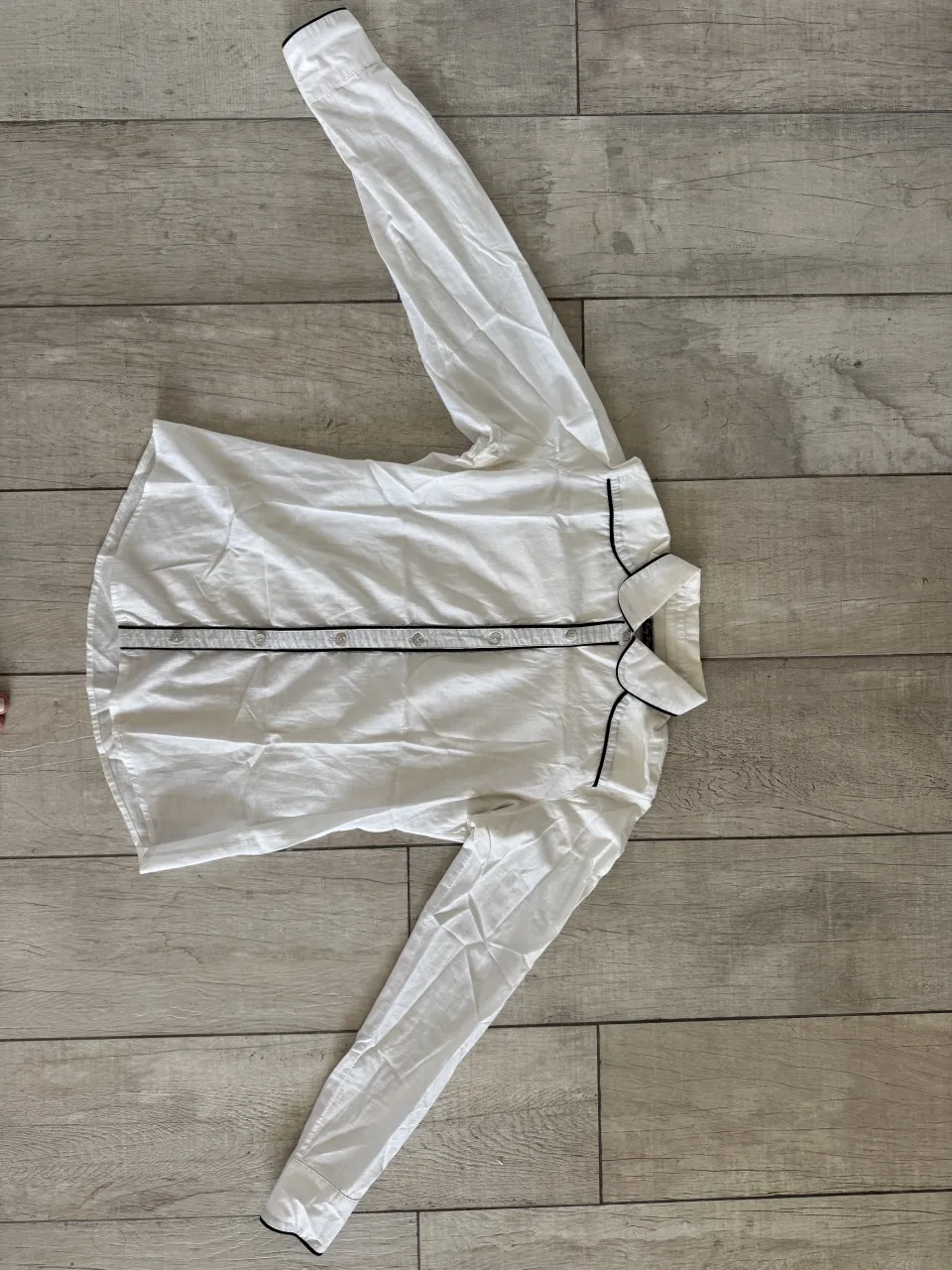 Camisa blanca de manga larga con vivos negros en cuello y puños. Posee botones al frente.