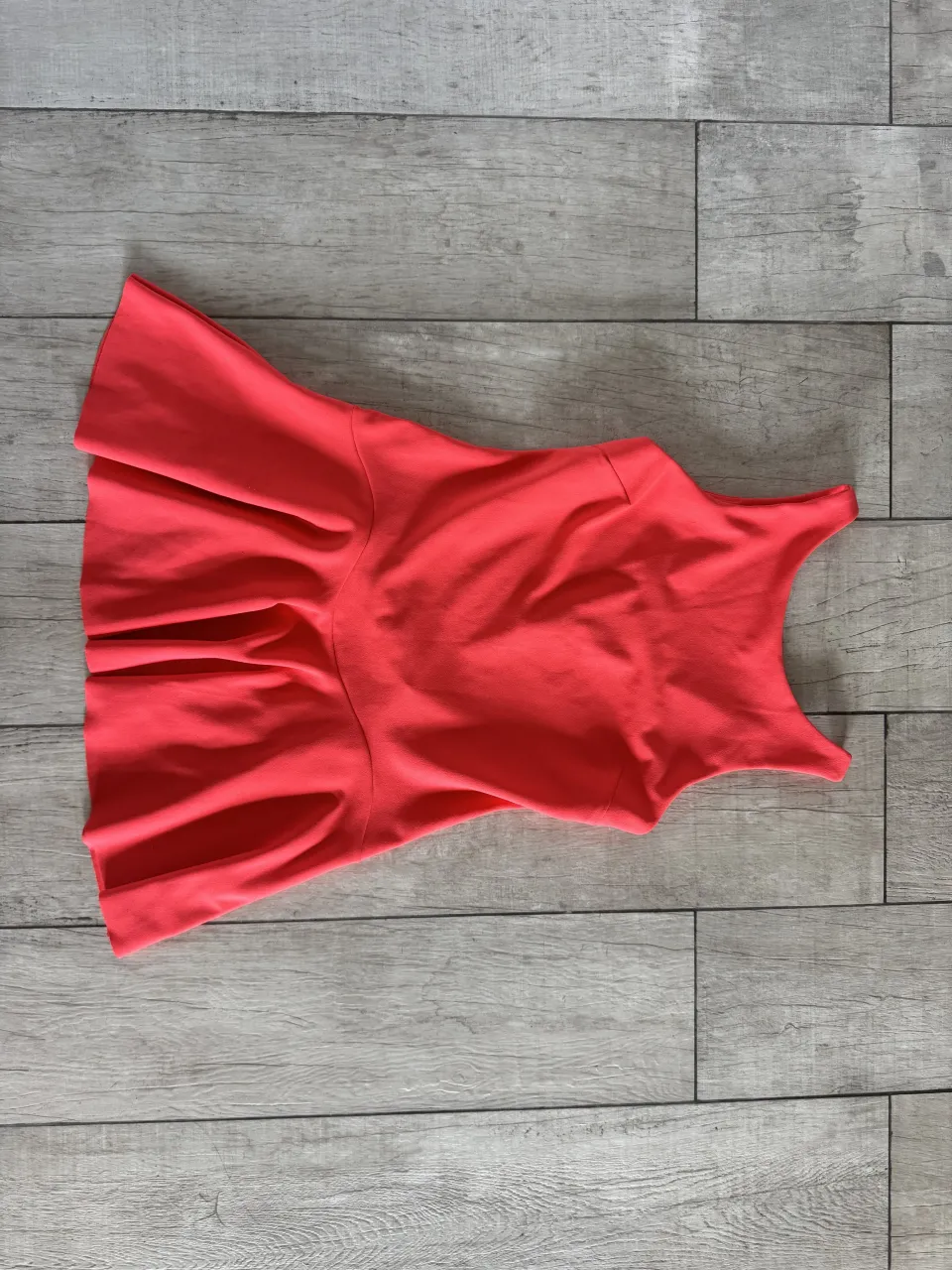 Vestido de color coral, sin mangas, con espalda en V y falda con pliegues.