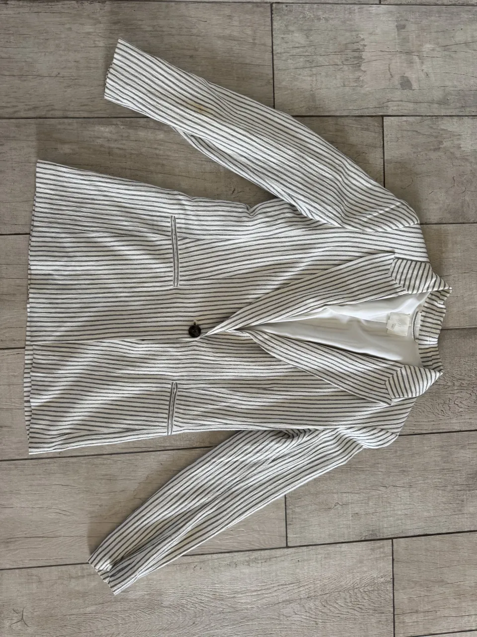 Blazer a rayas blancas y negras. Tiene dos botones al frente y dos bolsillos con solapa.