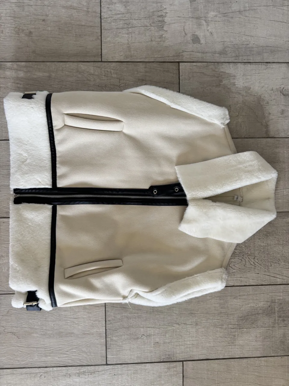 Campera de cuero sintético color crudo con forro de corderito blanco. Tiene cuello, puños y detalles en los bordes de corderito. Posee cierre metálico negro al frente y dos bolsillos laterales con solapa.