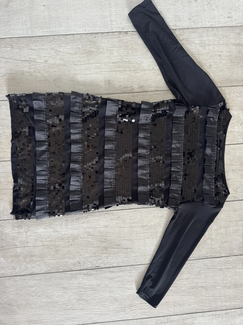 Vestido negro con mangas largas. El torso está adornado con tiras verticales de lentejuelas negras y cintas de satén.