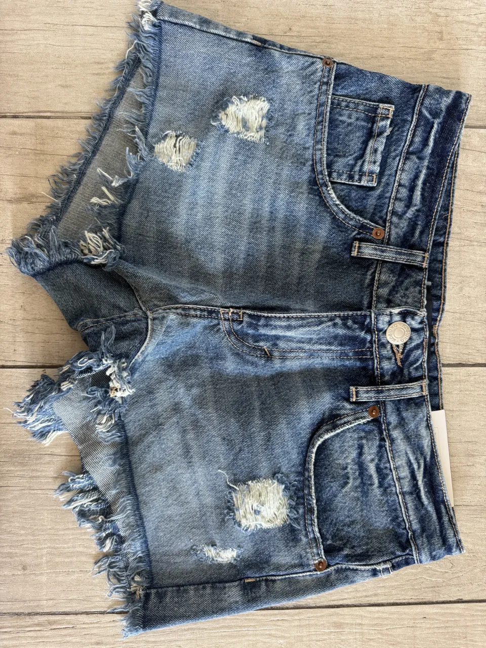 Shorts de jean azul con roturas y detalles desflecados en los bordes. Tienen bolsillos delanteros y traseros.