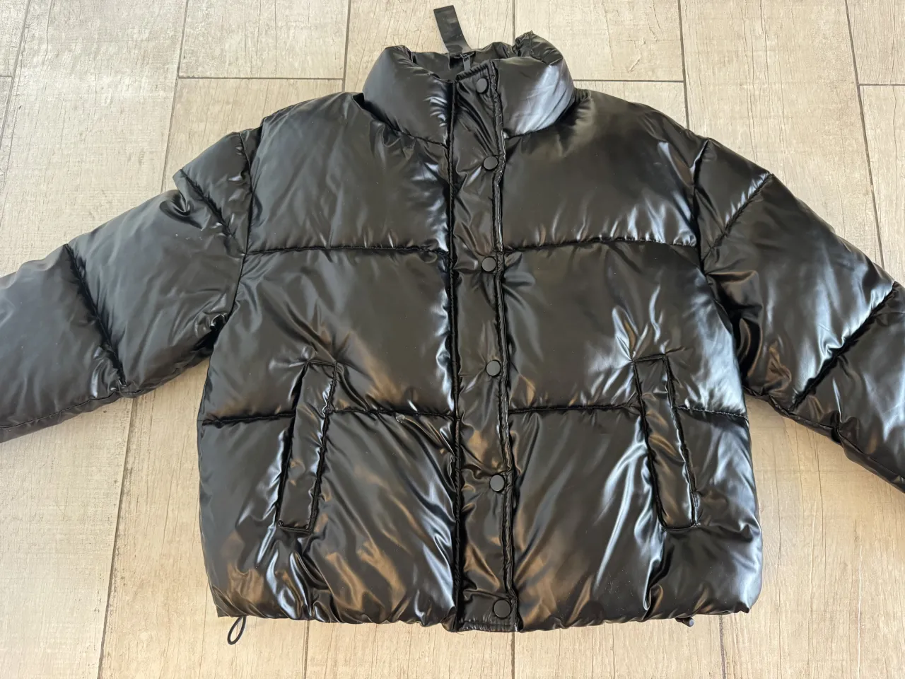 Campera puffer negra brillante con cuello alto y bolsillos frontales. Cierre de broches.
