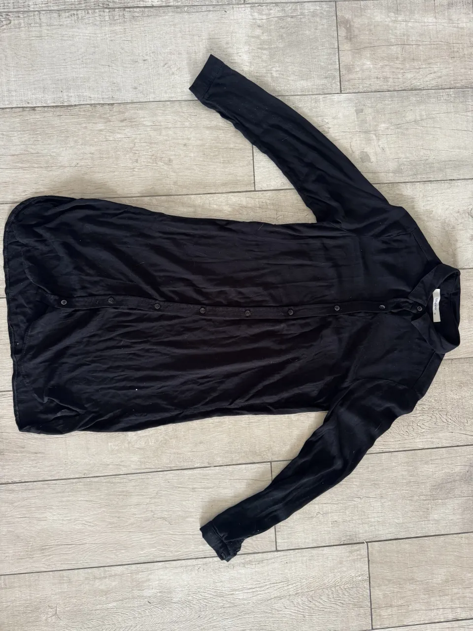 Camisa larga negra con botones al frente y mangas largas.