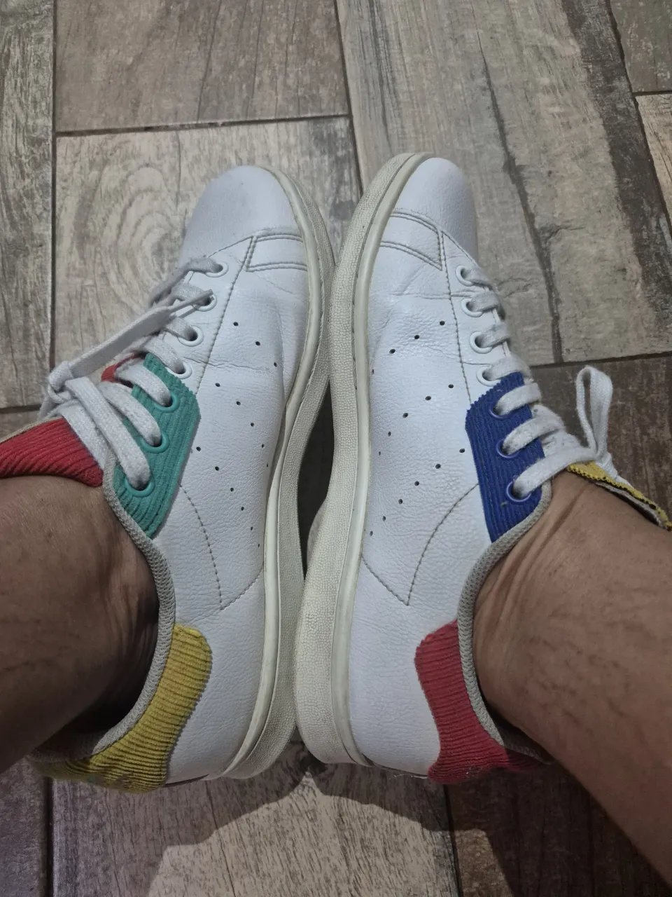 Zapatillas blancas de cuero con detalles de colores en el talón y en los laterales. Cordones blancos y suela de goma.