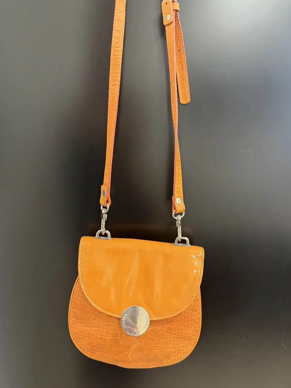 Cartera bandolera PRUNE naranja, con textura símil cocodrilo y solapa brillante. Interior de gamuza. Ideal para un look moderno y canchero.