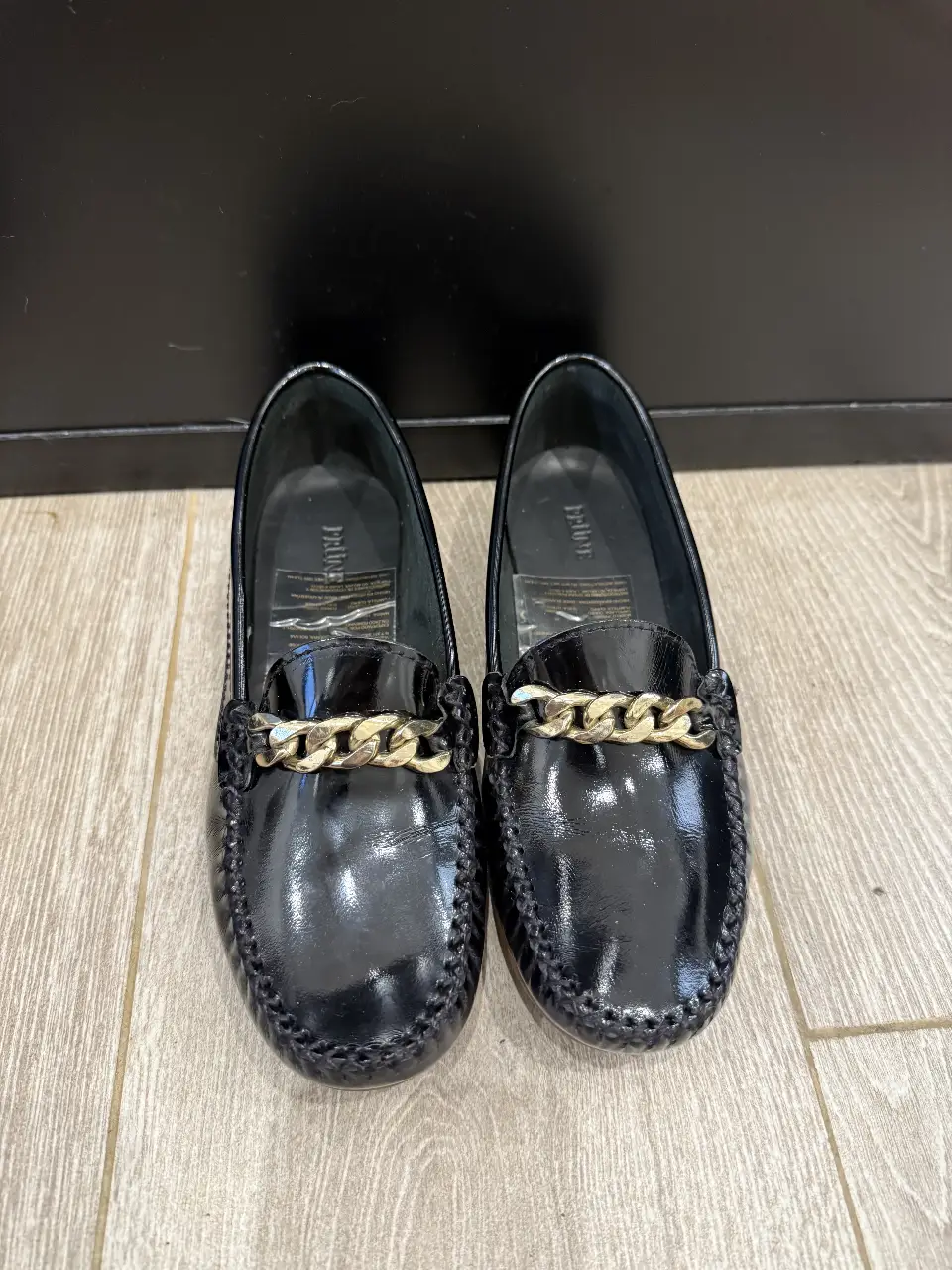 Mocasines de charol negro con detalle de cadena dorada. Diseño elegante y atemporal, ideales para un look sofisticado y cómodo.