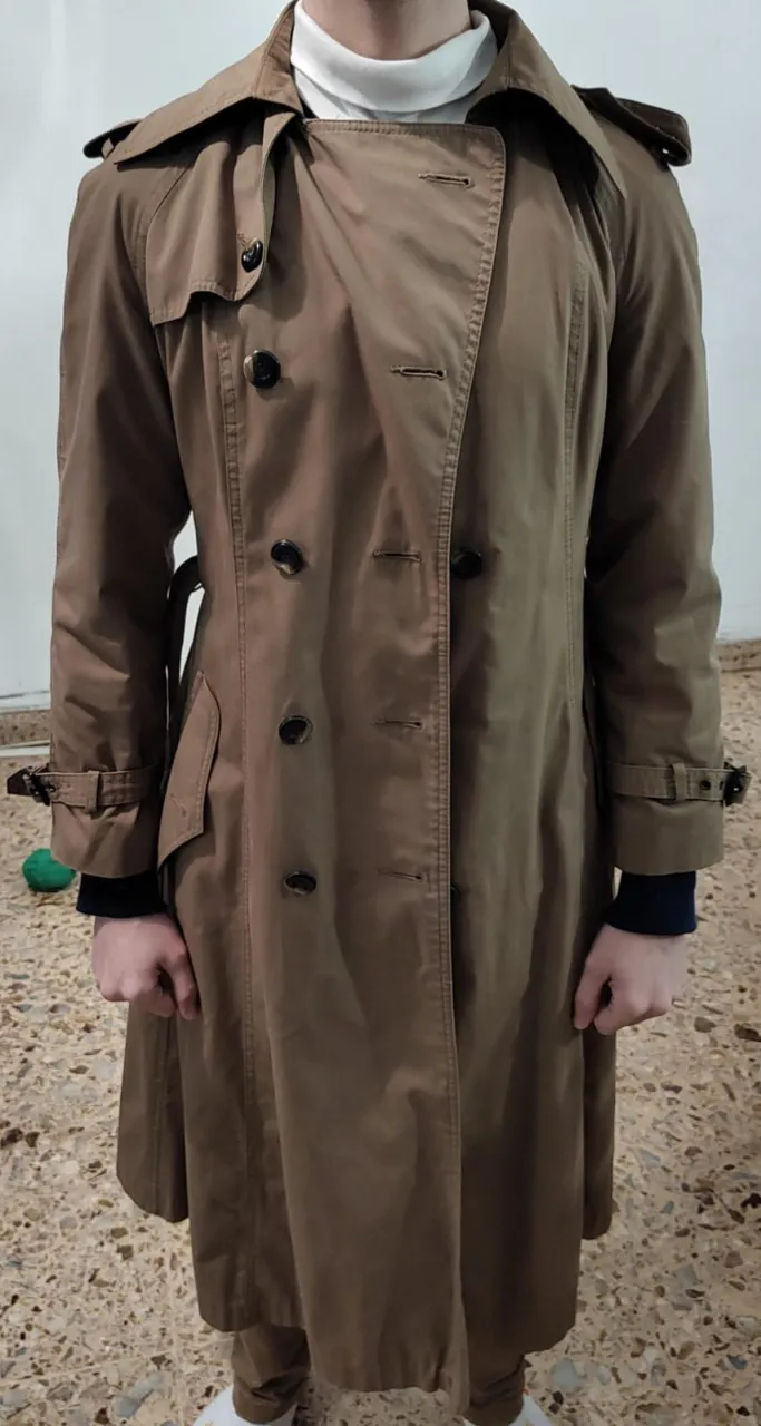 Trench coat marrón para hombre, largo, con doble botonadura y cinturón. Ideal para un look elegante y abrigado en otoño e invierno.