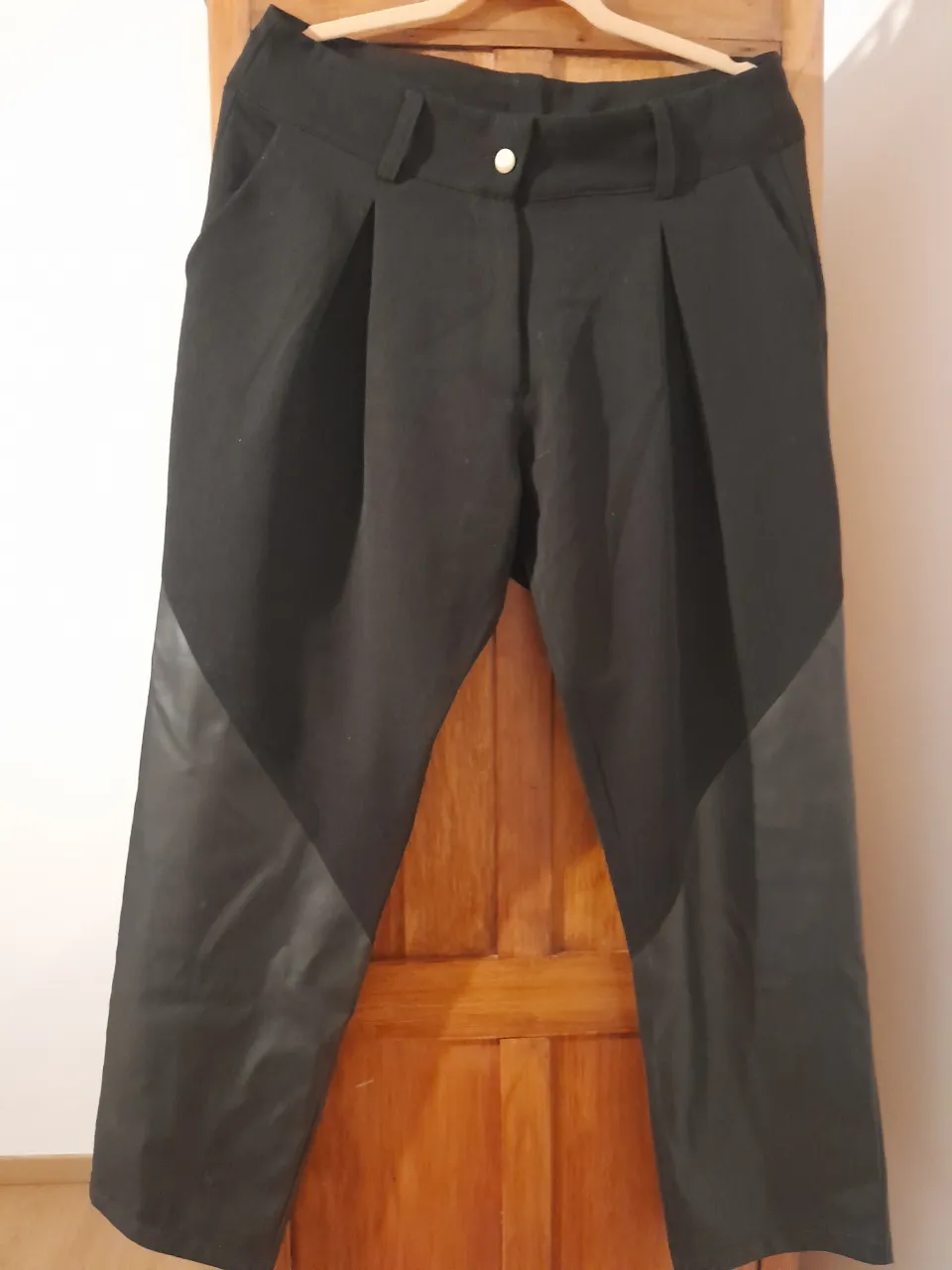 Pantalón negro con detalles de cuero sintético en la parte inferior. Diseño moderno con pinzas y corte recto, ideal para un look urbano y sofisticado. Perfecto para combinar con tops o blusas.