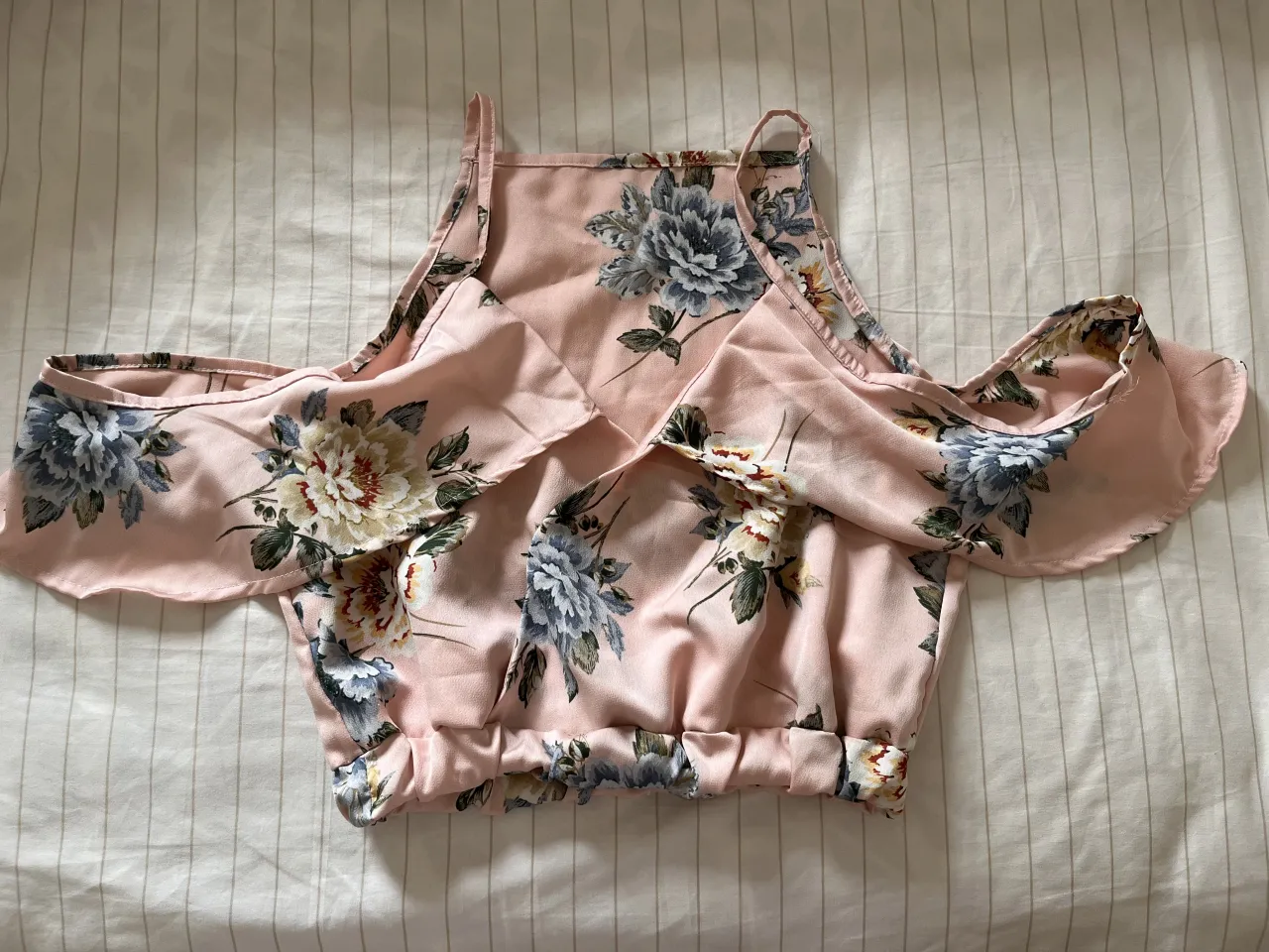 Top rosa con estampado floral en tonos azules y blancos. Posee breteles finos y mangas cortas con caida y volados.