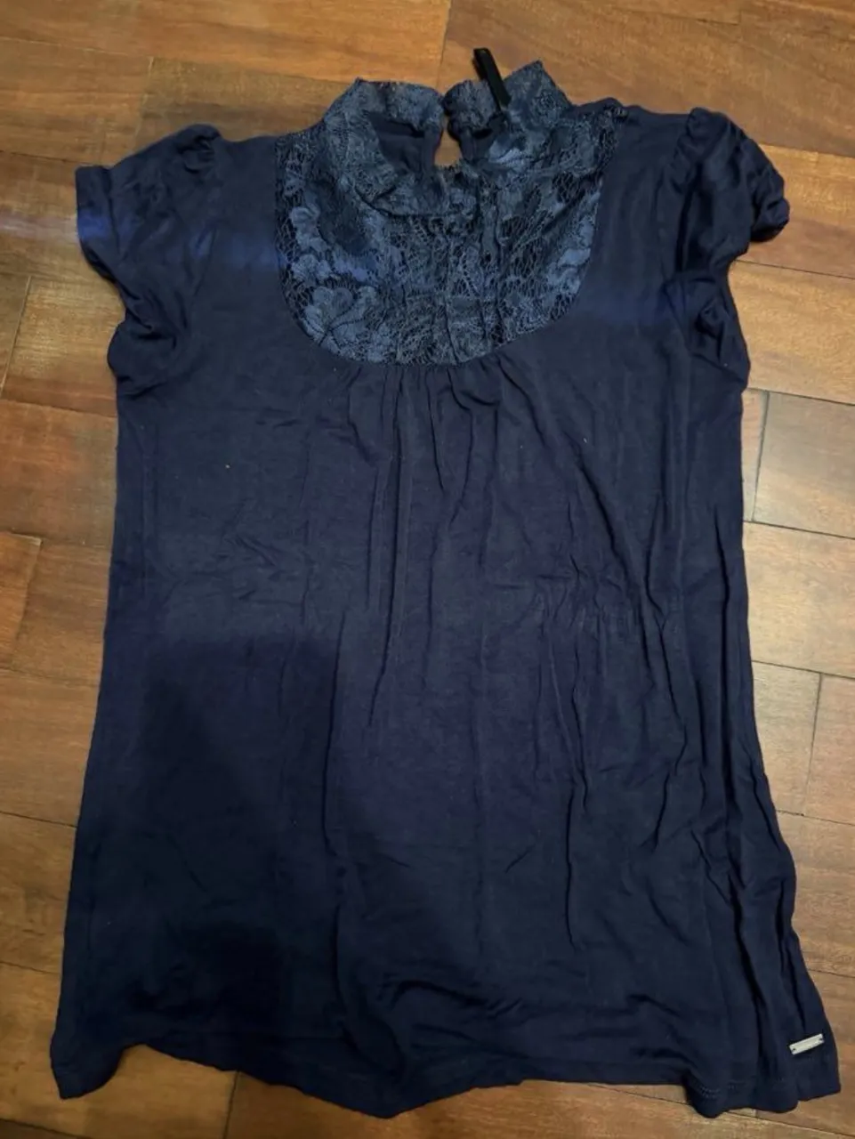 Remera azul marino con cuello alto y detalles de encaje floral en el frente. Mangas cortas. Ideal para un look elegante y casual.