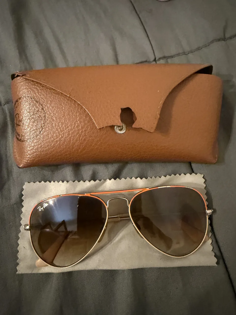 Lentes de sol Rayban estilo aviador, con marco metálico y detalles en naranja. Incluyen estuche de cuero marrón y paño de limpieza. Ver foto de los detalles 