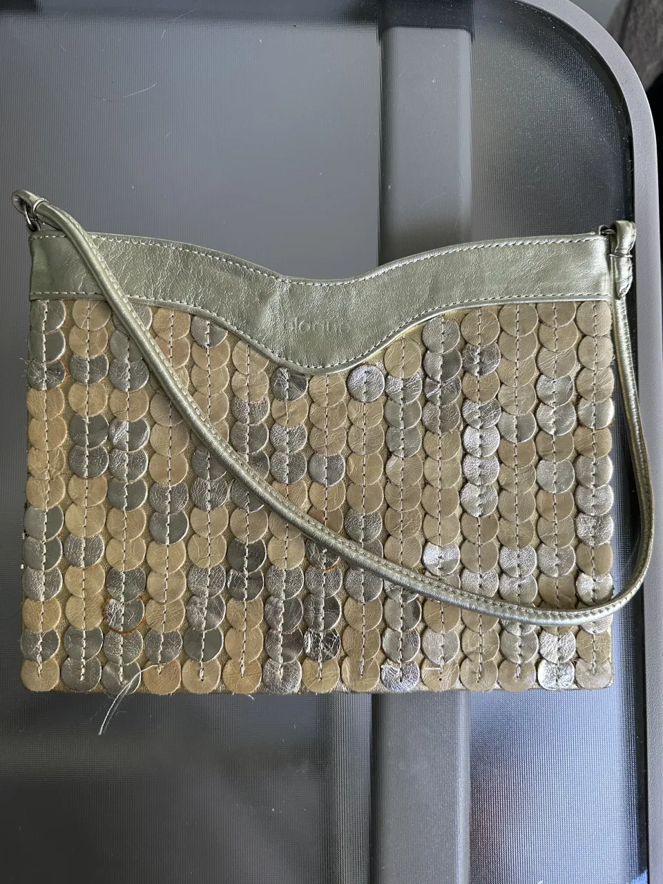 Cartera Blaqué de mano de cuero natural,con apliques circulares en dorado y plateado. Correa fina y cierre superior.