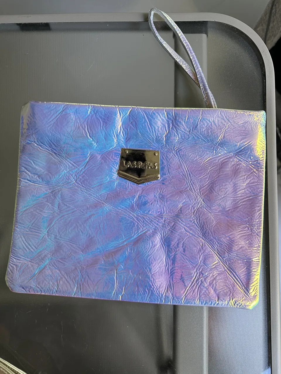 Cartera tipo clutch confeccionada en cuero natural iridiscente con textura arrugada. Posee un detalle metálico con el logo de la marca en la parte frontal y una tira de mano.Falta logo en la parte trasera, adjunto foto.