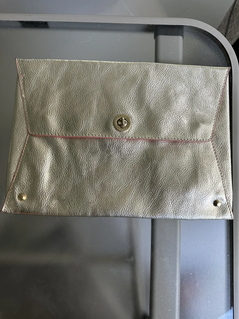 Cartera Prune de cuero natural,tipo sobre en color dorado con detalles en rosa. Posee un cierre metálico dorado con el logo de la marca.