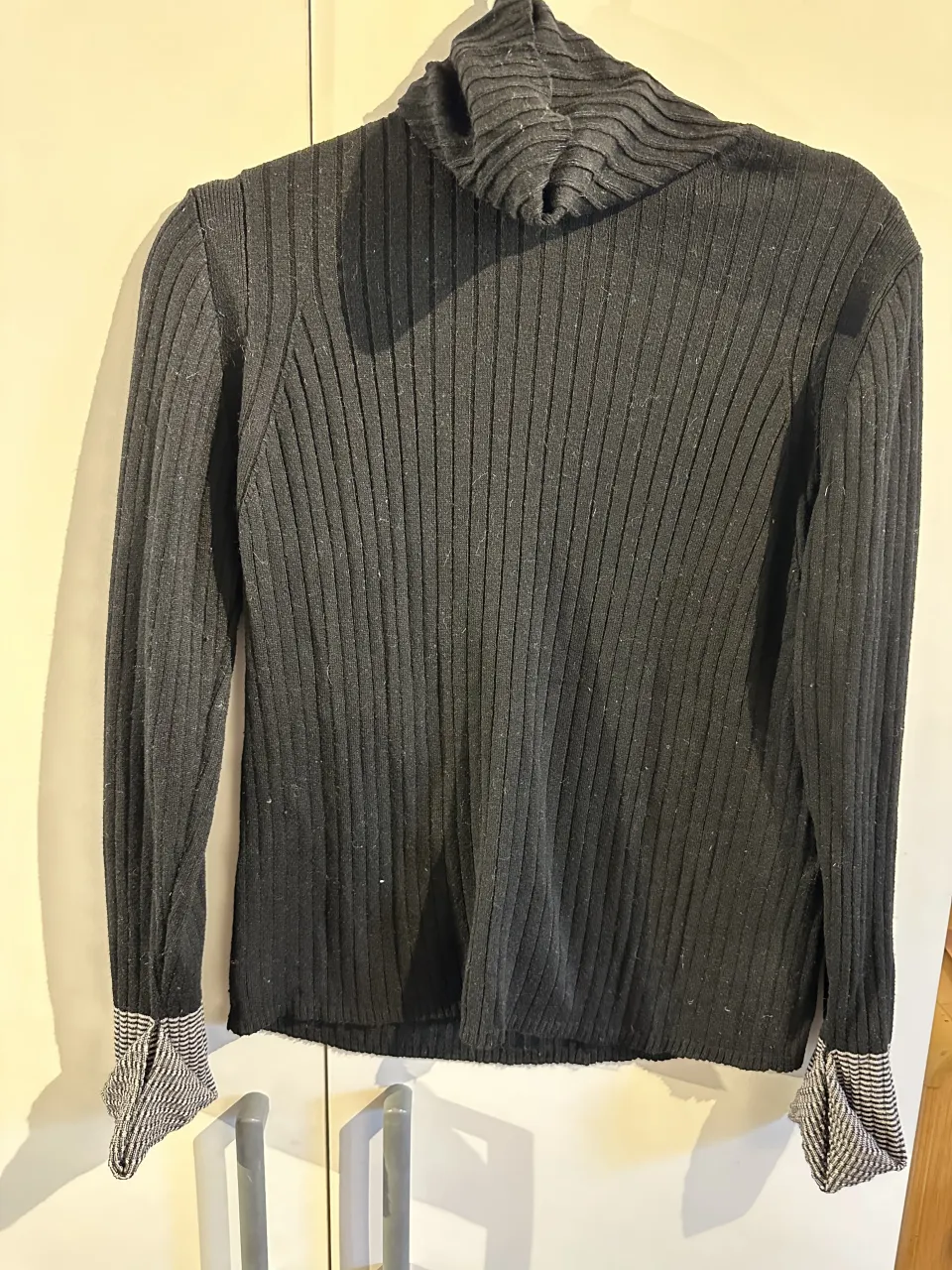 Sweaters Vitamina,de lana y alpaca negro con cuello alto y puños a rayas. Tiene un detalle metálico con el logo de la marca en la espalda.