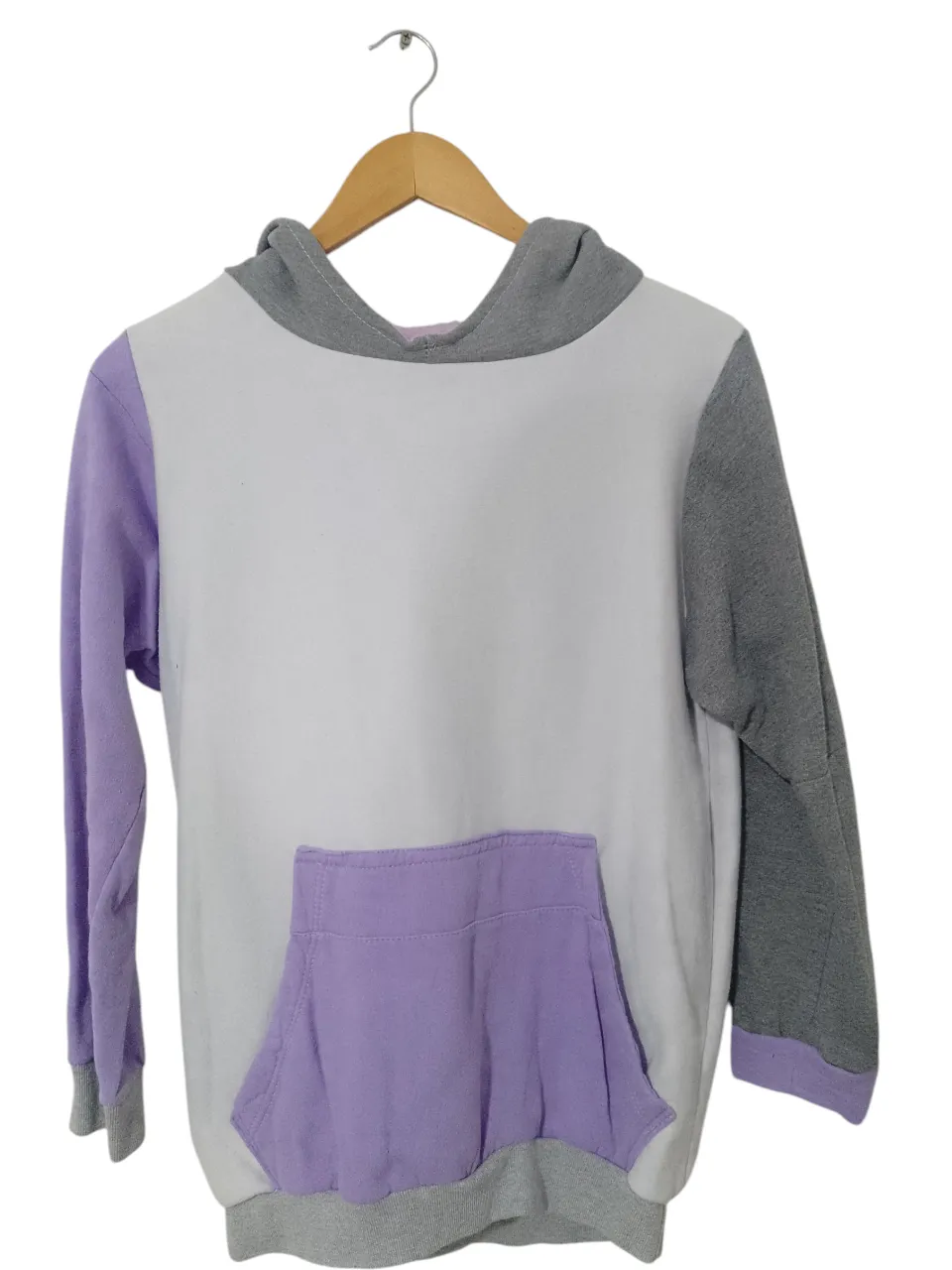 Buzo canguro para mujer, con capucha y bolsillo delantero. Diseño en bloques de color blanco, gris y lila. Ideal para un look casual y cómodo.