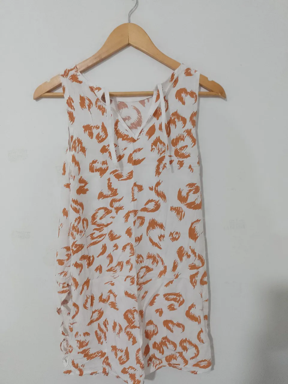 Blusa/vestido sin mangas de mujer, con estampado de diseño abstracto en tonos naranja sobre fondo blanco. Cuello en V con detalle de lazos. Ideal para un look fresco y casual.