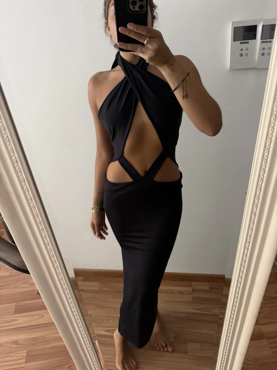 Vestido negro largo con escote halter cruzado y recortes en la cintura y abdomen.