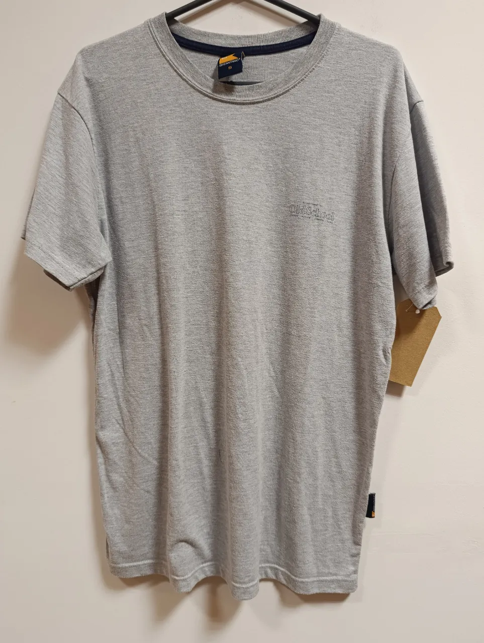 Remera gris de manga corta con cuello redondo. Presenta un pequeño logo bordado en el frente. Ideal para un look casual y cómodo.