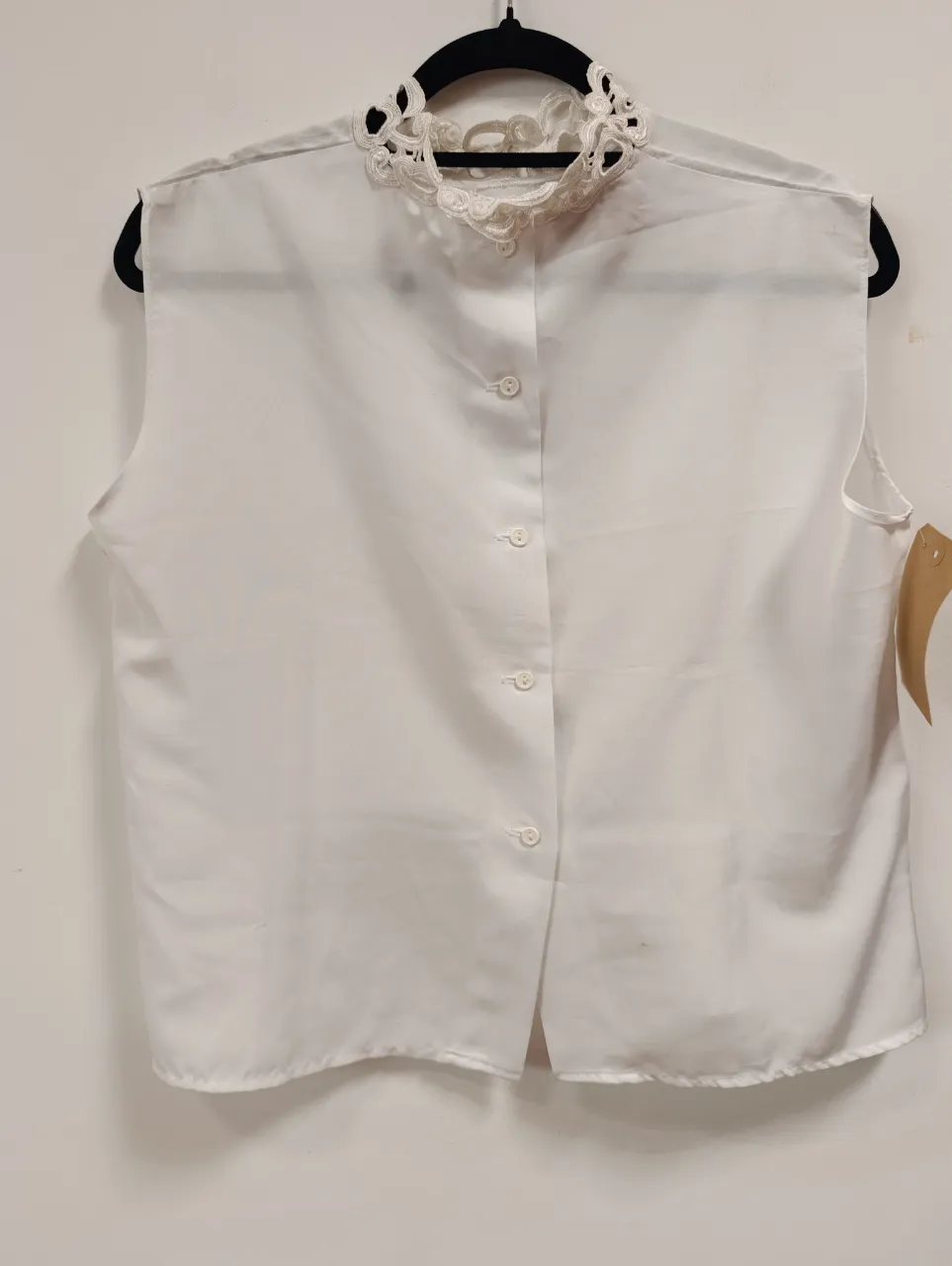 Blusa blanca sin mangas con cuello alto y detalles de encaje. Posee botones en la parte trasera.