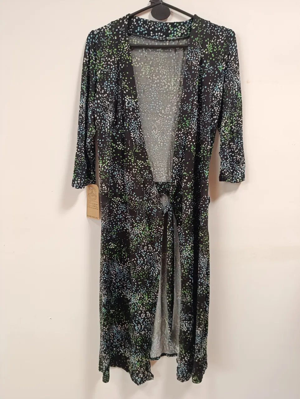 Kimono largo estampado con flores en tonos verdes, blancos y celestes sobre fondo negro. Posee mangas 3/4 y se ata con un lazo en la cintura. Ideal para usar sobre un traje de baño o como prenda de vestir liviana.