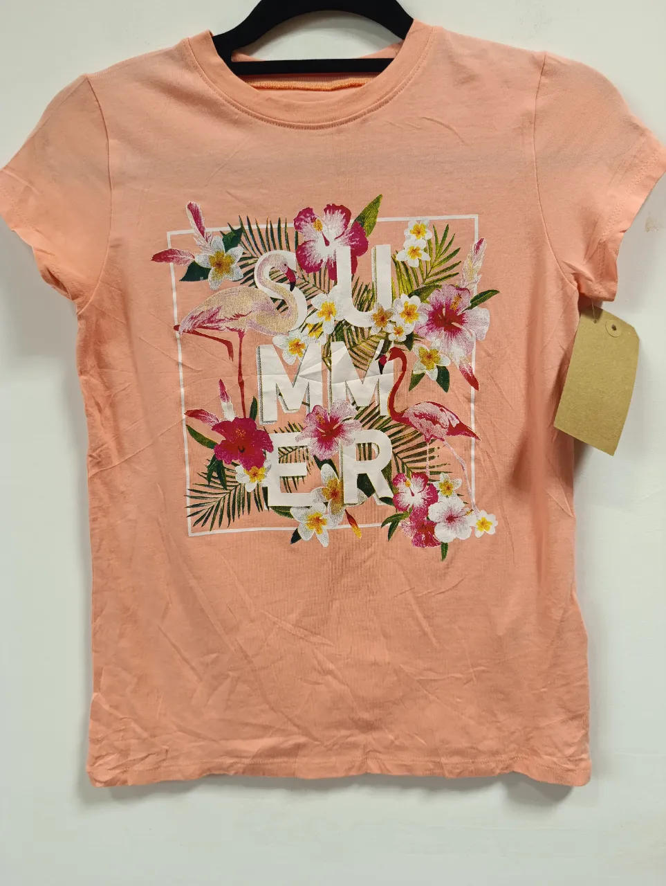 Remera de algodón color salmón con estampa "SUMMER" rodeada de flores tropicales y flamencos. Ideal para un look fresco y playero.