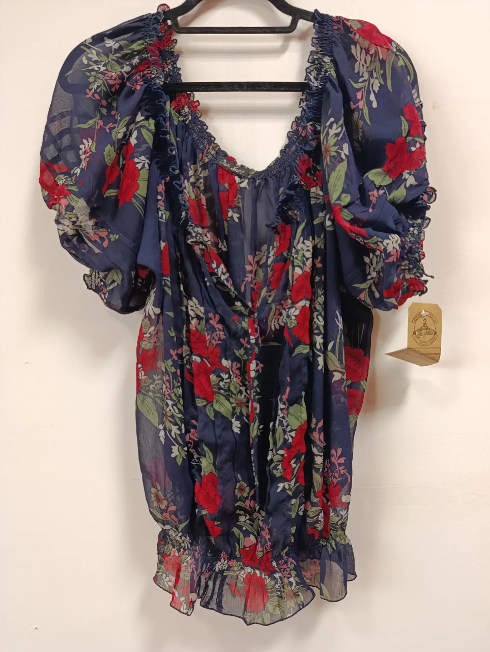 Blusa vaporosa con estampado floral en tonos azules y rojos. Posee detalles de elástico en cuello y puños, y volados en el borde inferior. Ideal para un look fresco y femenino.