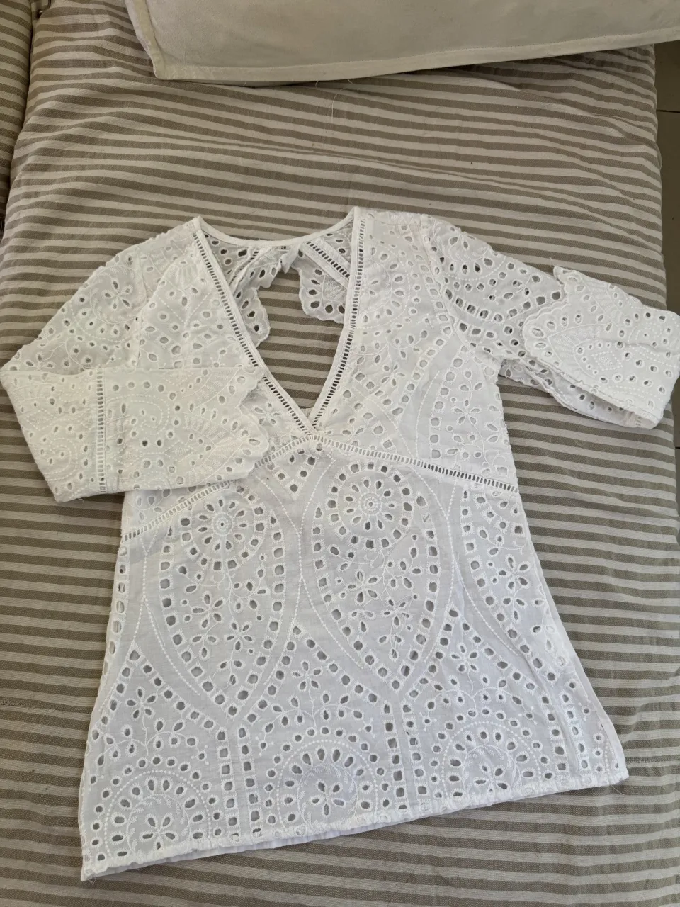 Blusa blanca con mangas largas y escote en V. Posee detalles de bordado y recortes en toda la prenda. La espalda tiene un recorte en forma de corazón.