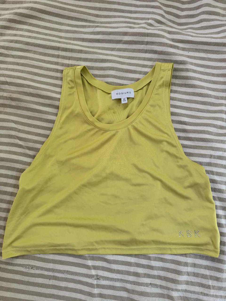 Musculosa deportiva color amarillo pastel con brillos en la parte inferior del frente.