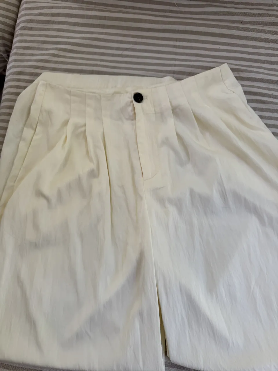 Pantalón blanco con pinzas en la parte delantera y un botón negro en la cintura.