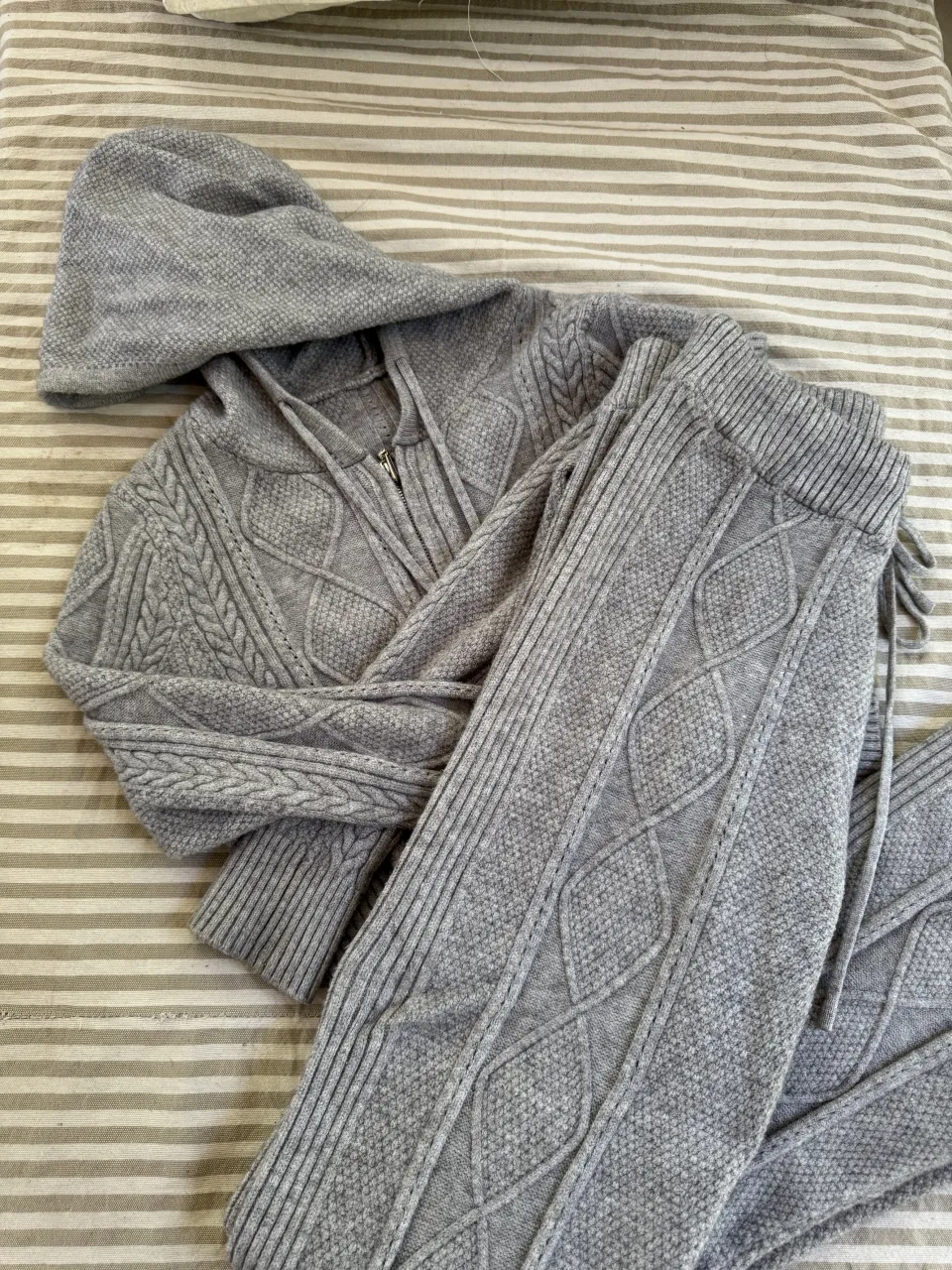 Conjunto de buzo con capucha y pantalón de tejido gris con trenzas. El buzo es corto y tiene cierre.