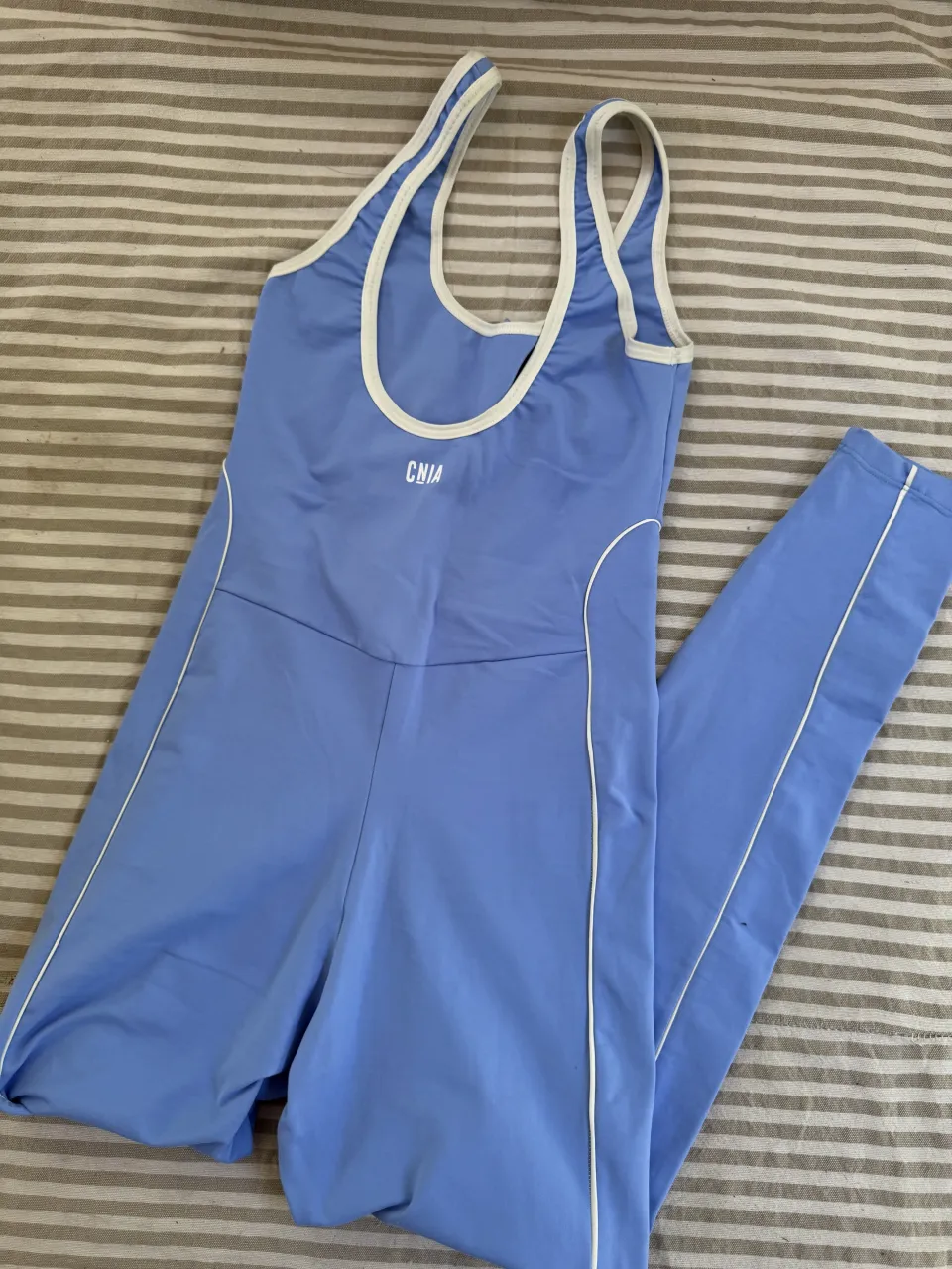 Mono deportivo azul claro con vivos blancos. Escote redondo y breteles finos. Posee un logo blanco en el frente.