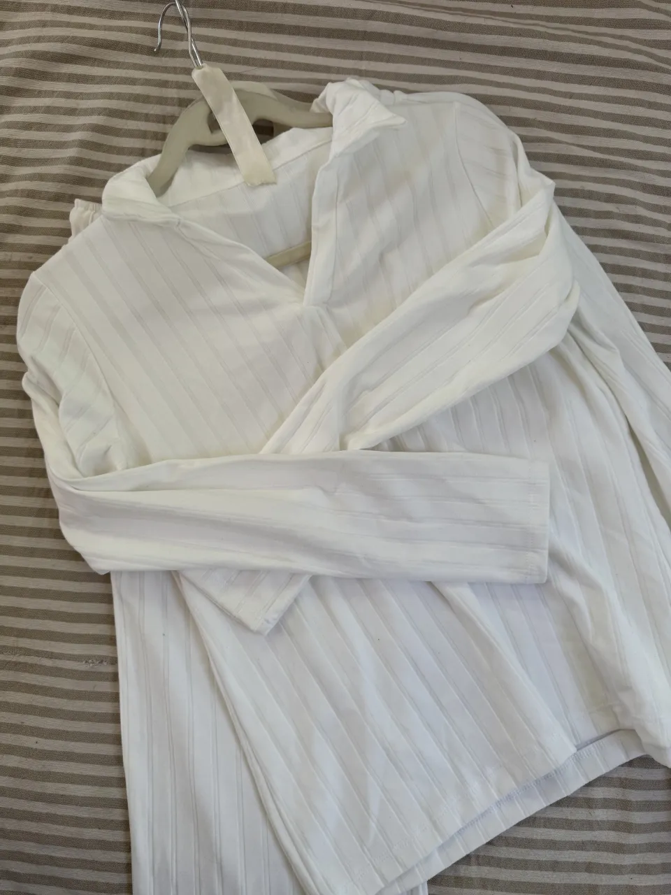 Conjunto de pijama blanco de dos piezas. Incluye una remera de manga larga con cuello escote en V y un pantalón largo. Ambas prendas tienen un diseño de finas rayas verticales.
