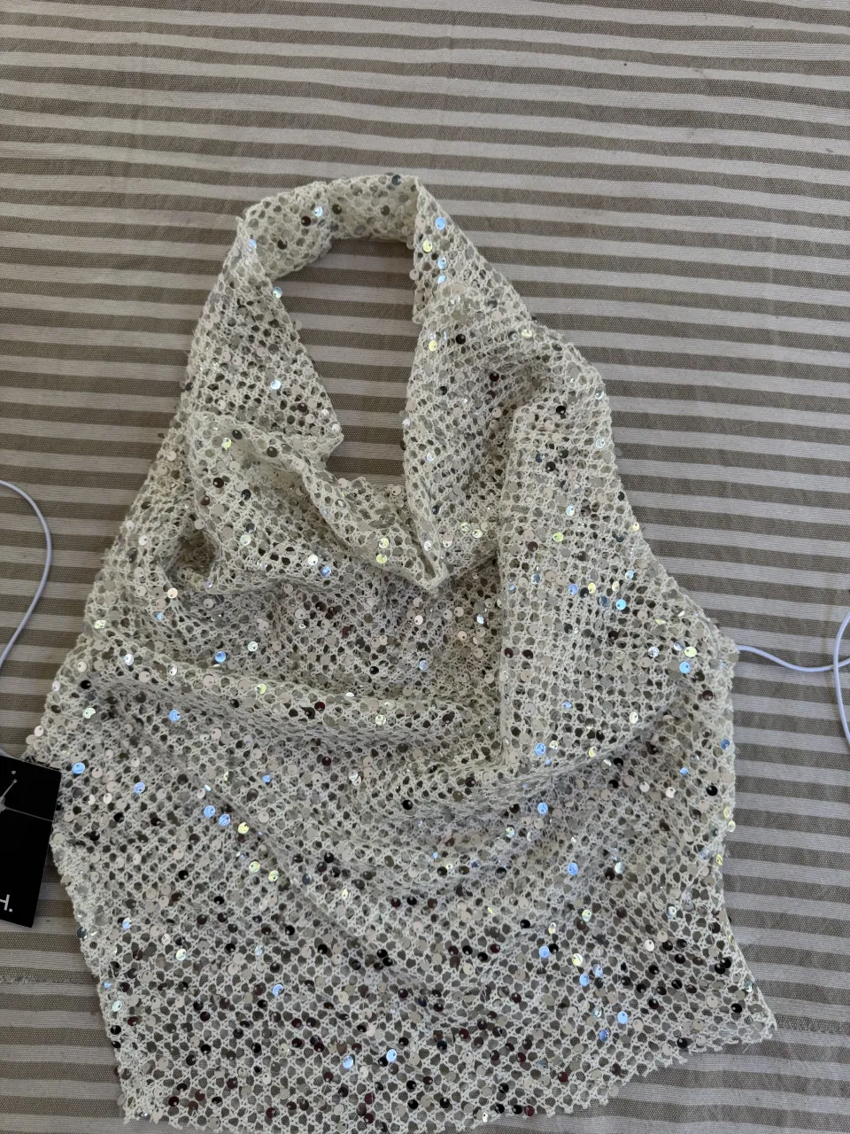 Top blanco con lentejuelas plateadas y detalles calados. Posee cuello halter y espalda descubierta.