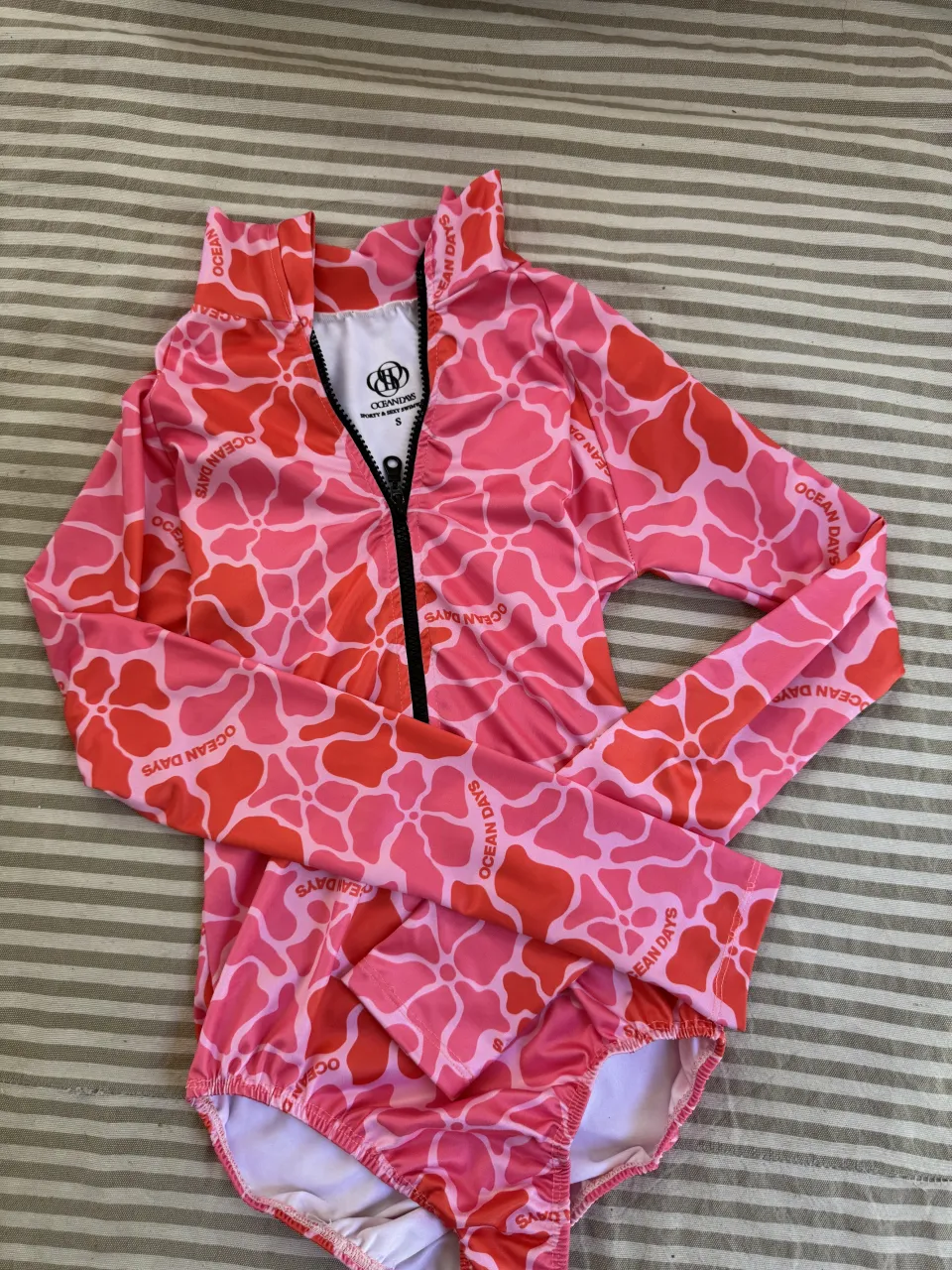 Enterito de baño manga larga con cuello alto y cierre al frente. Estampado floral en tonos de rosa y coral.