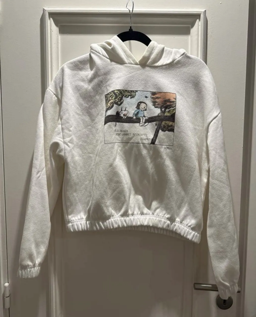 Buzo blanco con capucha y estampa de ilustración en el frente. Posee puños y cintura elastizados.