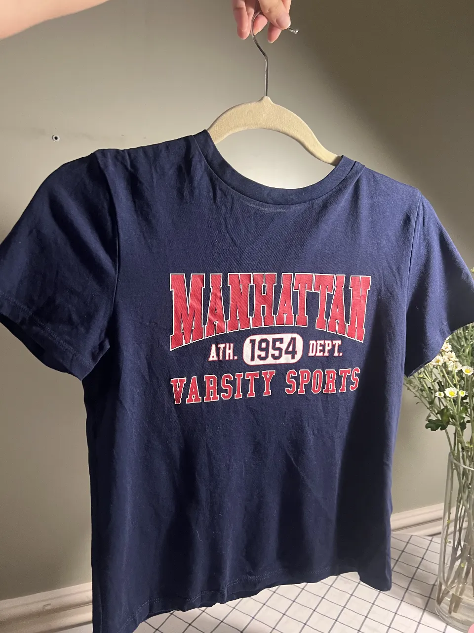Remera azul marino con estampa "MANHATTAN ATH. 1954 DEPT. VARSITY SPORTS" en rojo y blanco. Ideal para un look casual y deportivo.