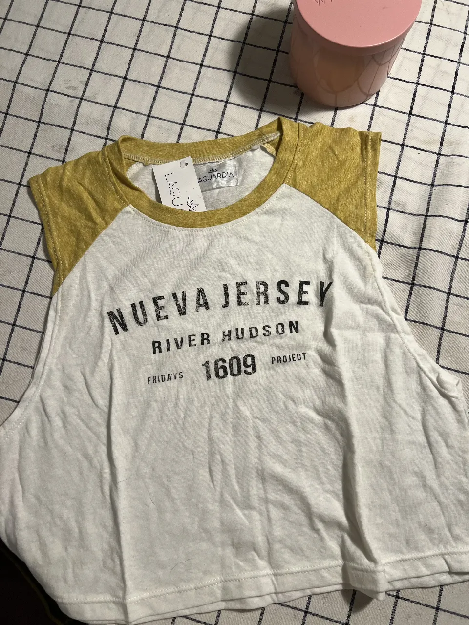 Musculosa crop blanca con mangas y cuello en color amarillo ocre. Estampado "NUEVA JERSEY RIVER HUDSON FRIDAYS 1609 PROJECT" en negro. Ideal para un look casual y urbano.