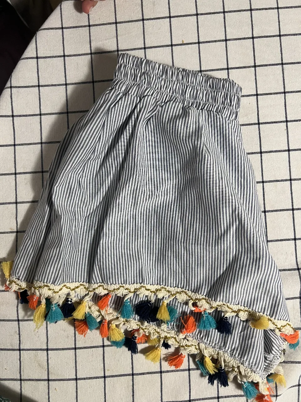 Pollera corta a rayas blancas y azules, con elástico en la cintura y detalle de pompones de colores en el ruedo. Ideal para un look fresco y divertido.