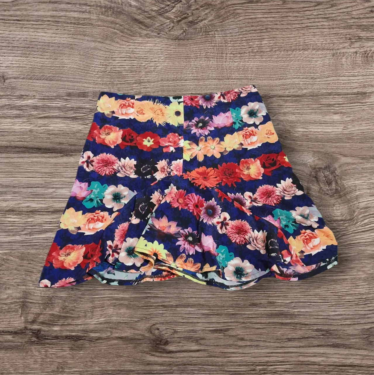 Pollera larga con estampado floral en tonos vibrantes sobre fondo azul marino. Diseño con volados y vuelo, ideal para un look bohemio y femenino.