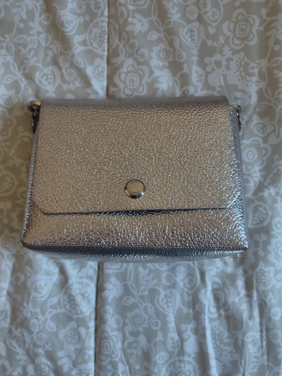 Cartera bandolera plateada con textura, ideal para salidas. Marca Prune.